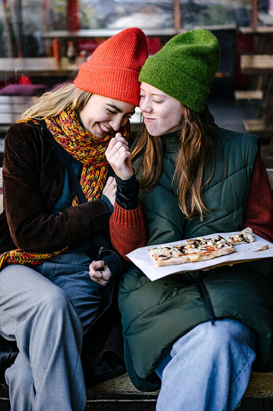 Zwei Freundinnen mit bunten Mützen genießen Sushi zusammen.