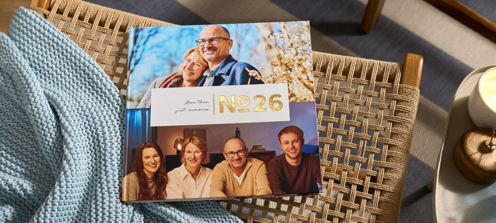 CEWE FOTOBUCH „N°26“ mit Fotos eines Paares und einer Familie von vier Personen auf einem geflochtenen Stuhl mit blauer Decke.