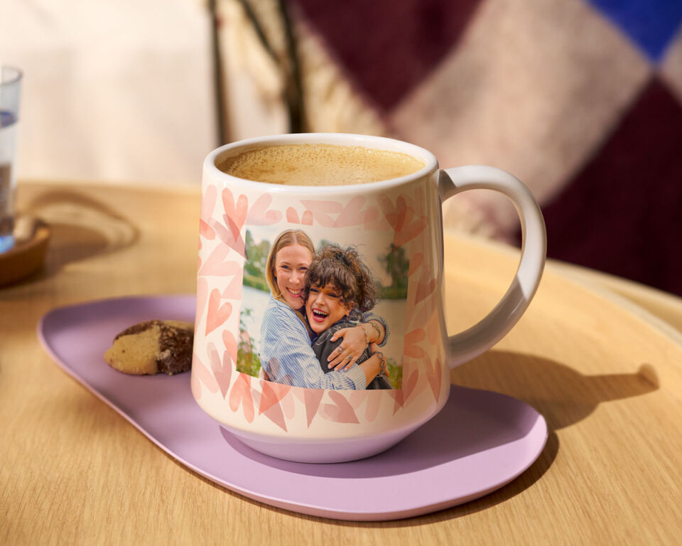 Personalisierte Tasse mit Foto von zwei lachenden Freundinnen auf einem Tisch mit Kaffee und Gebäck.