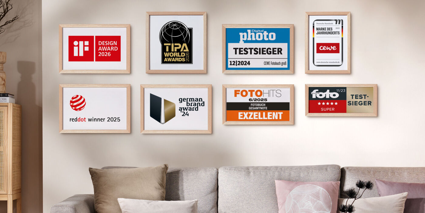 Mehrere gerahmte Auszeichnungen und Testsiegel von CEWE hängen an einer Wand über einem Sofa und stehen für geprüfte Qualität und Vertrauen
