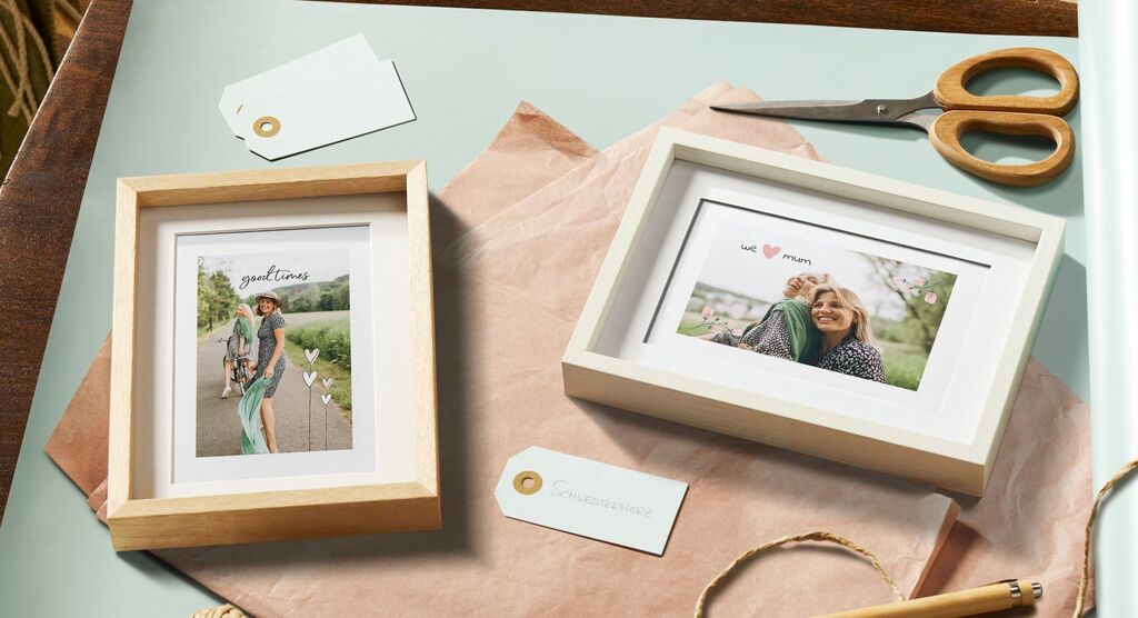 Zwei schöne Bilderrahmen mit personalisierten Fotos auf einem Tisch, umgeben von einer Schere und Etiketten