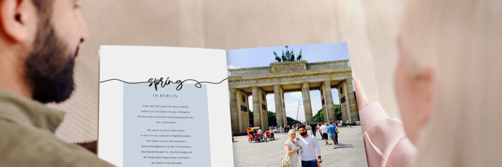 Ein Paar betrachtet ein CEWE Fotobuch mit Bildern vom Brandenburger Tor.
