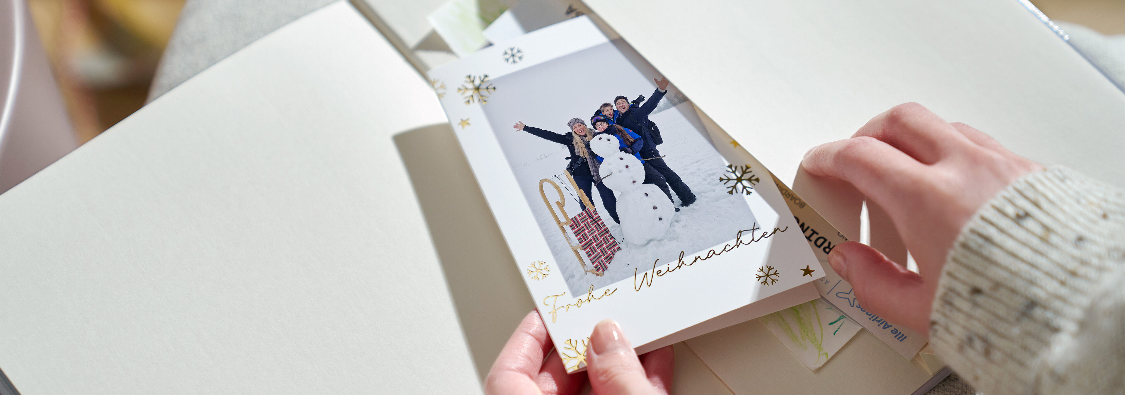 Eine Hand hält eine Weihnachtskarte mit einem Foto von Freunden und einem Schneemann.