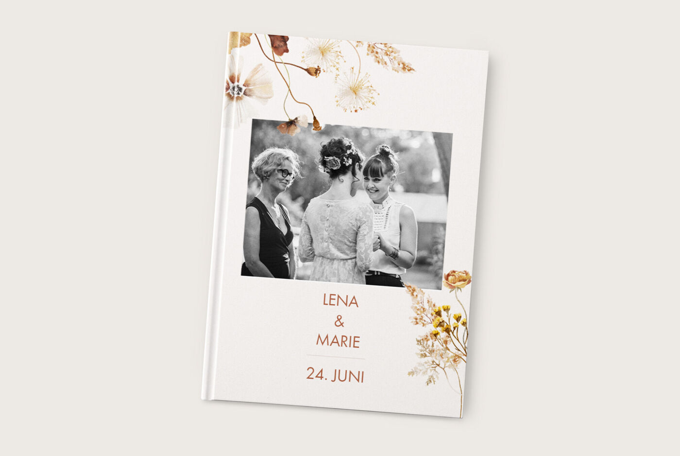 Ein individuelles CEWE Fotobuch mit floralen Akzenten. Es zeigt die Namen "Lena & Marie" und das Datum "24. Juni" auf dem Cover. Drei Frauen stehen im Bild und teilen einen fröhlichen Moment.
