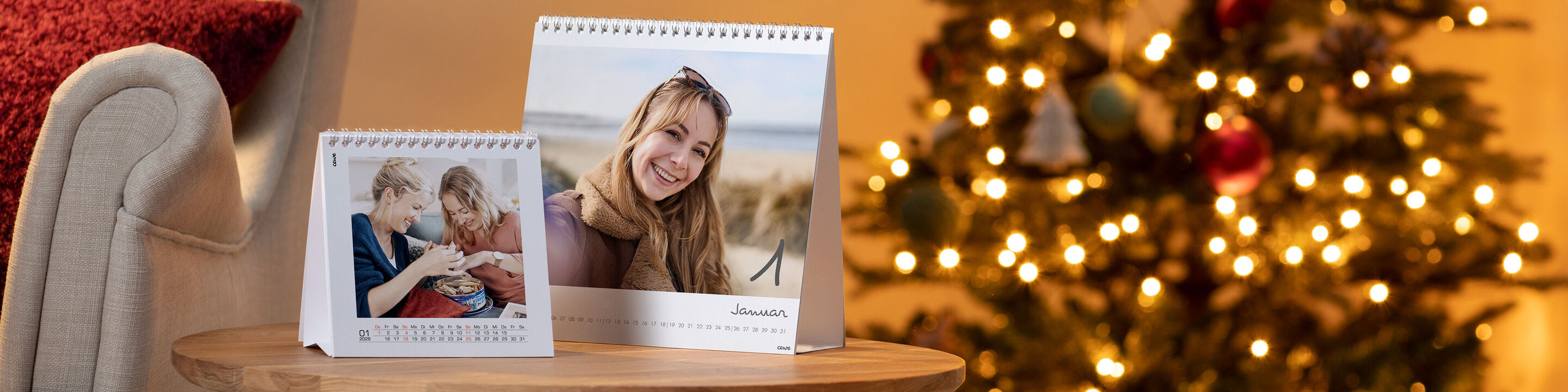 Zwei CEWE Fotokalender auf einem Holztisch vor einem weihnachtlich geschmückten Baum