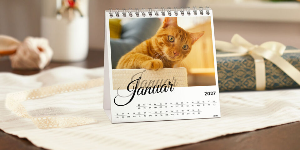 Tischkalender von CEWE mit einem Foto einer orangefarbenen Katze, daneben ein Geschenk mit Schleife