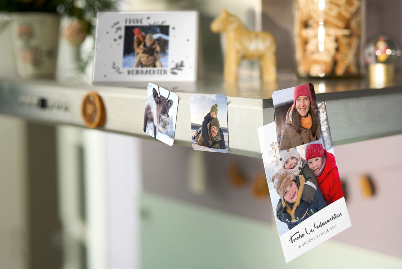 CEWE Grußkarten und Fotomagnete mit winterlichen Familienfotos an metallischer Dunstabzugshaube