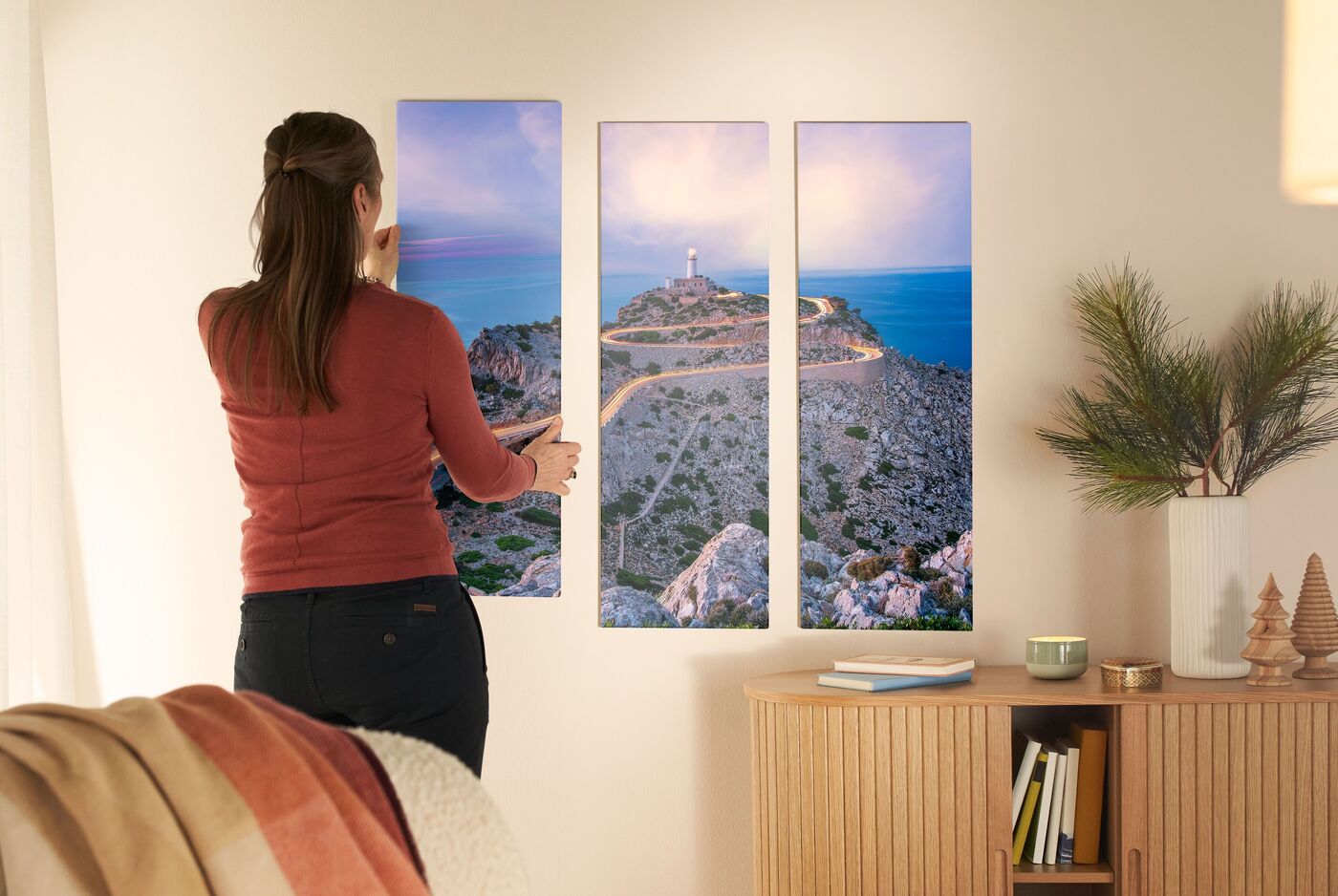 Eine Frau gestaltet ein Wandbild mit einem Leuchtturm, das an einer Wand hängt