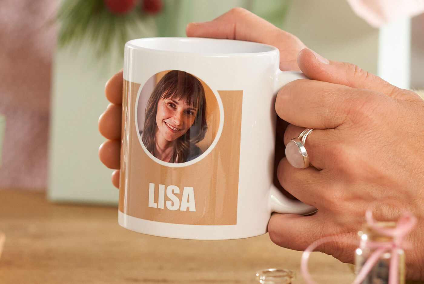 Eine Frau sitzt an einem Tisch und hält eine Fototasse in der Hand, gestaltet mit einem Foto und der Aufschrift „Lisa“.