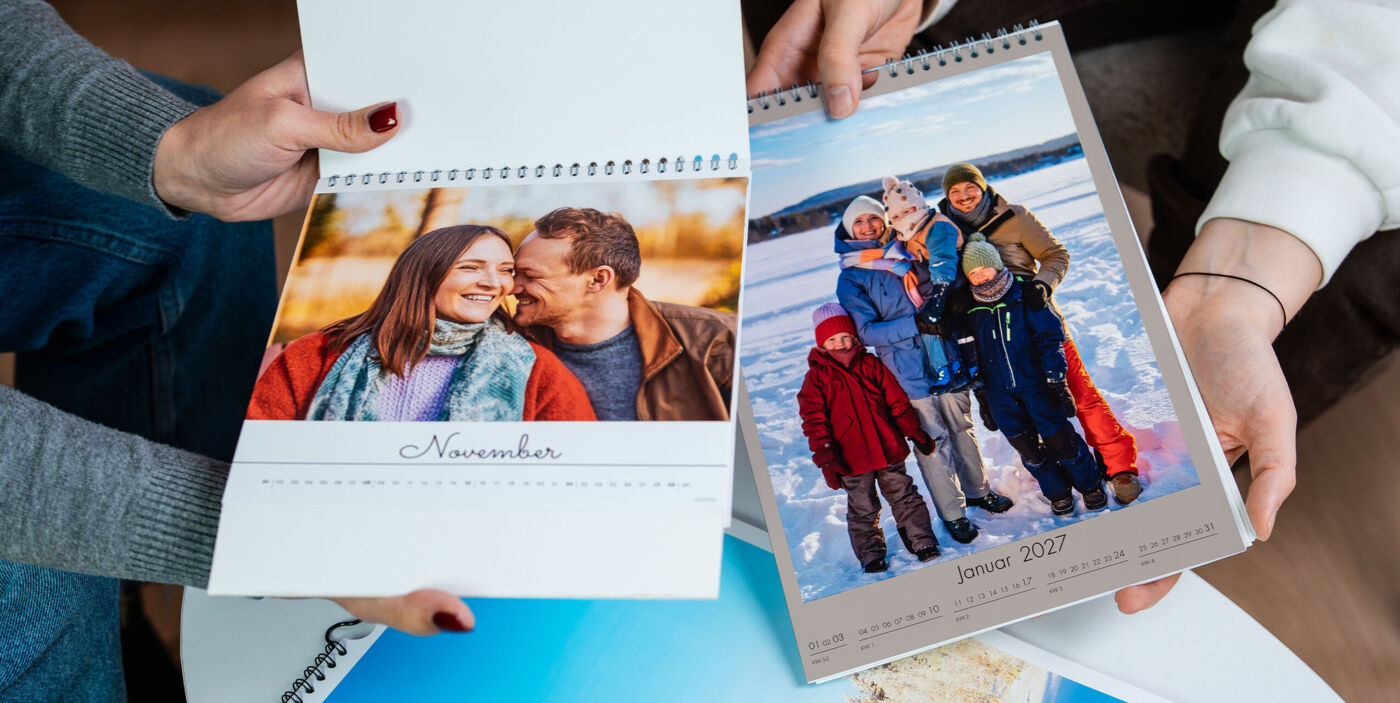 Eine Person hält zwei CEWE Fotokalender, einer mit einem Paar und der andere mit einer Familiengruppe im Schnee.