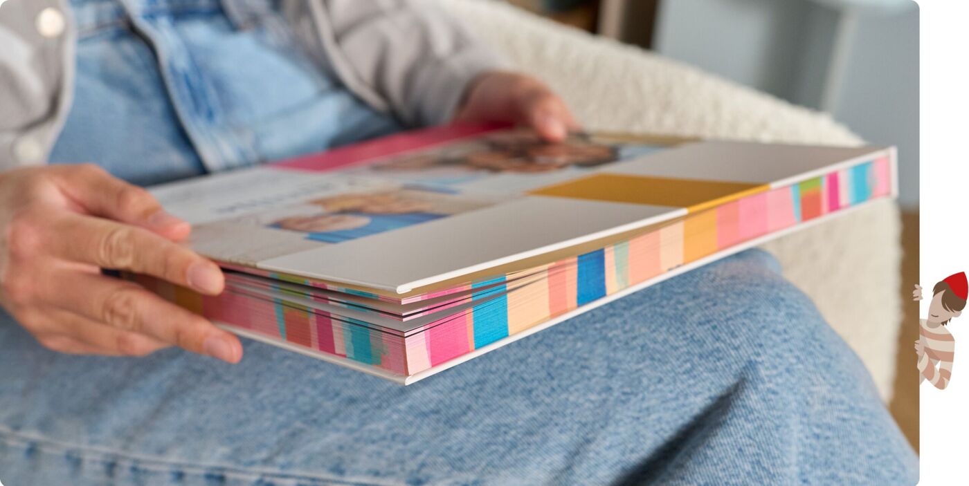 Person hat ein personalisiertes CEWE FOTOBUCH mit Farbschnitt mit buntem Streifenmotiv an den Seitenkanten.