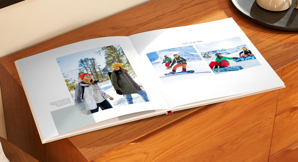 Ein offenes Fotobuch auf einem Tisch, zeigt Winterurlauber beim Ski und Snowboard fahren.