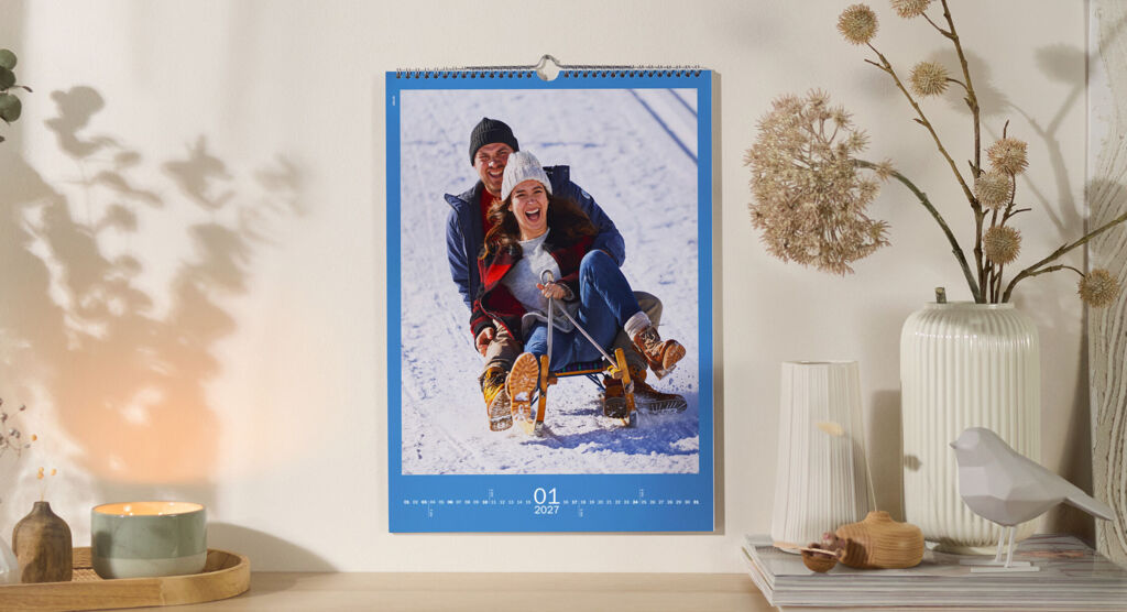 CEWE Fotokalender mit Schlittenfahrt im Schnee an Wand über winterlich dekoriertem Regal