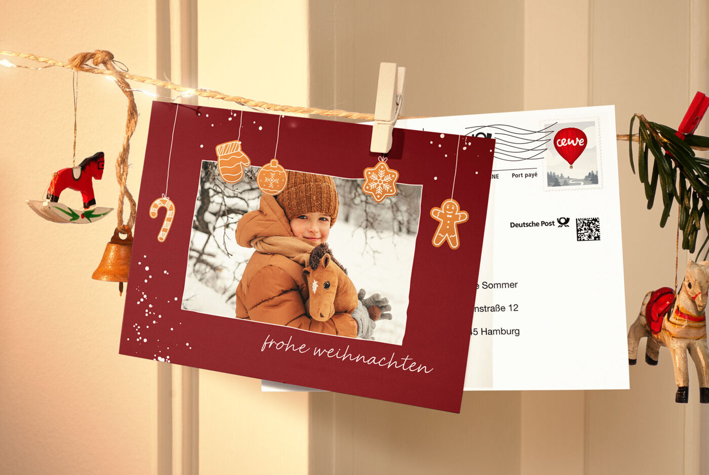 Ein Kind in warmer Kleidung hält ein Stoffpferd und lächelt. Daneben hängt eine rote Weihnachtskarte.