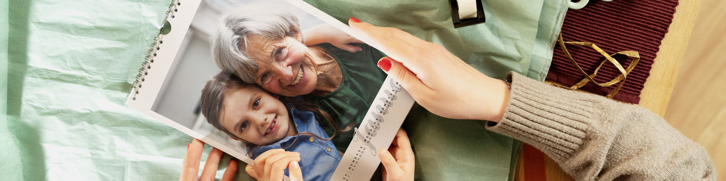 Person hält einen CEWE Fotokalender mit einem Foto von Kind und älterer Person über Geschenkpapier.