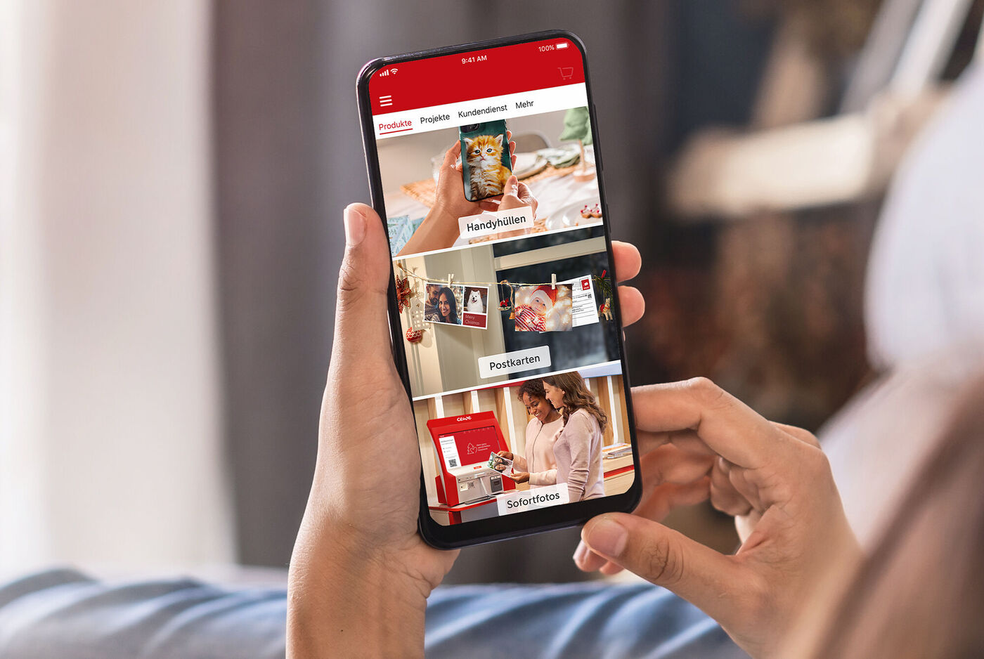 Person hält Smartphone, auf dem die CEWE Fotobuch App zu sehen ist, mit verschiedenen Optionen zur Gestaltung