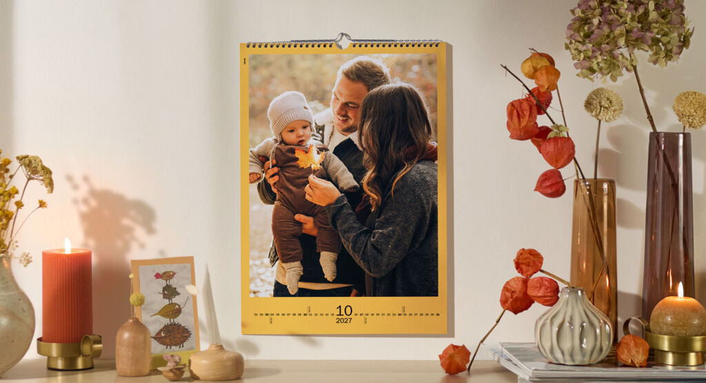 CEWE Fotokalender mit herbstlichem Familienfoto an Wand über herbstlich dekoriertem Regal mit Kerzen und Blumen