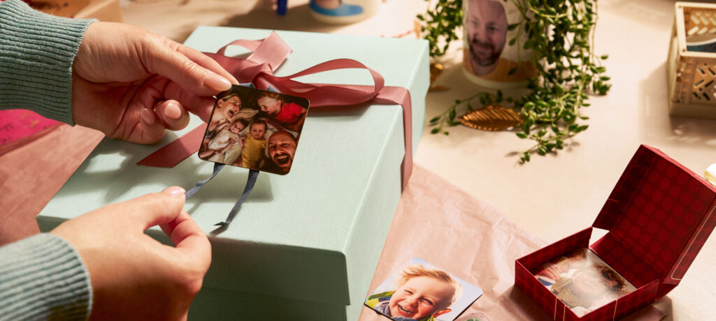 Eine Person befestigt zwei Magneten mit Fotomotiven als Anhänger an einem Geschenk.