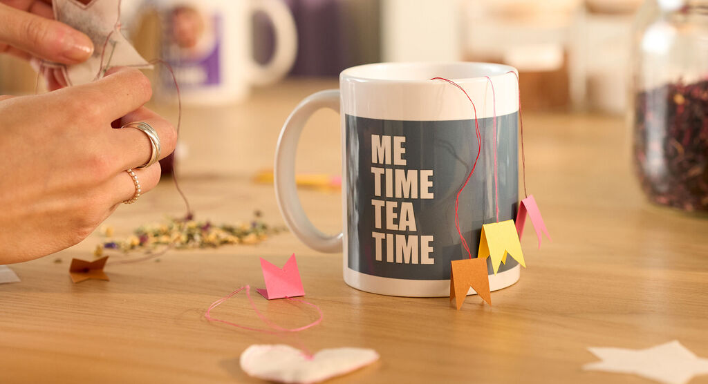 Tasse mit dem Text Me Time Tea Time und bunten Teebeuteln auf Holztisch.