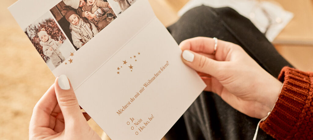 Eine Person hält eine CEWE Grußkarte mit festlichem Design in den Händen. Das Innere der Karte ist mit goldenen Sternen verziert und hat liebevolle Botschaften.