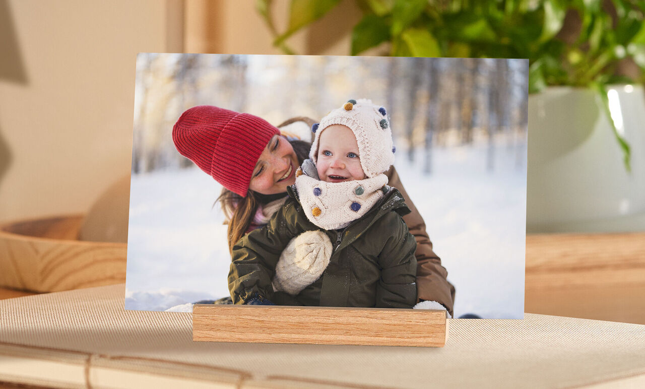 Eine Mutter umarmt ihr Kind in winterlicher Landschaft, beide lächeln und genießen den Moment.