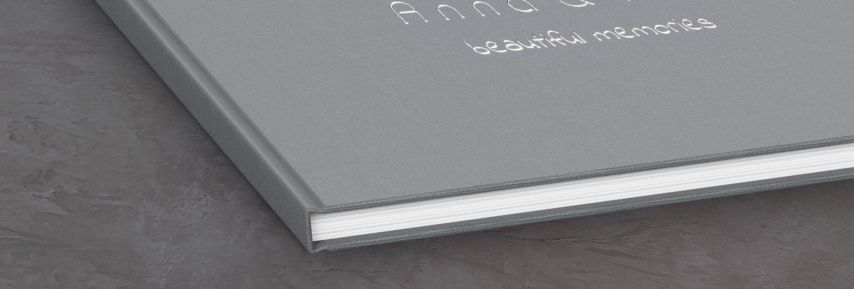 Graues CEWE Fotobuch mit dem Titel 'Anna &' und dem Untertitel 'beautiful memories' auf einem Tisch.