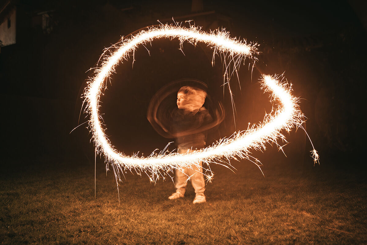 Eine Person, die mit einem Feuerwerkskörper in einem Kreis leuchtet, im Dunkeln.