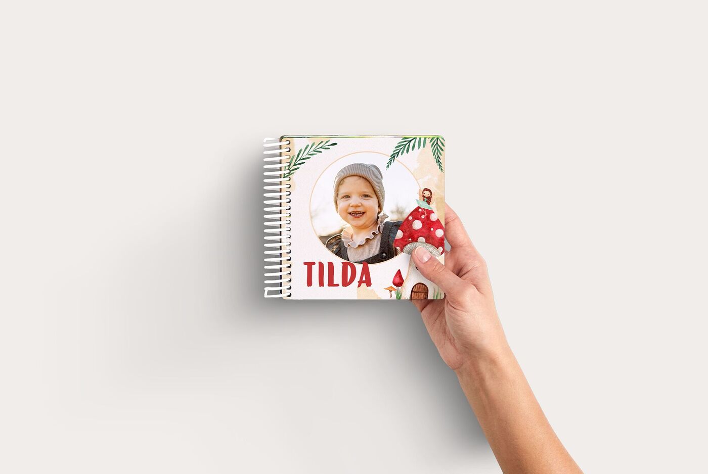 Hand hält ein CEWE FOTOBUCH mit dem Titel Tilda im Feenland, gestaltet mit Pilz- und Pflanzenmotiven