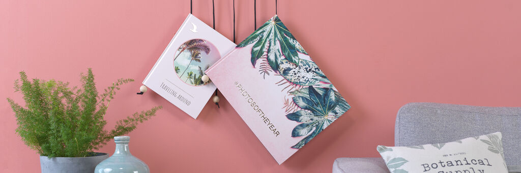 Zwei stilvolle Fotobücher hängen an einer Wand mit starker Farbe. Das eine zeigt botanische Illustrationen, das andere ein klares Design mit sanften Farben.