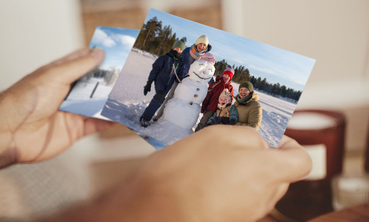 Eine glückliche Familie hält zwei Fotos in den Händen, eines von einem Winterlandschaft mit Schnee und eines vom Bau eines Schneemanns. Freude und schöne Erinnerungen strahlen aus ihren Gesichtern.