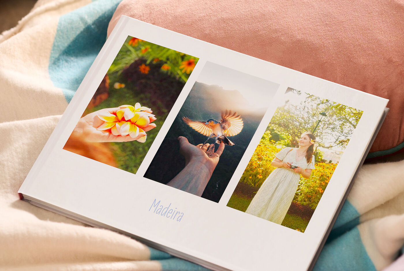 Offenes CEWE FOTOBUCH liegt auf einer Decke und zeigt Naturfotos mit Blüten, Vogel und sonnigem Garten