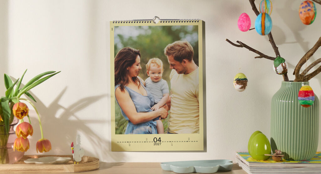 CEWE Fotokalender mit fröhlicher Familie an Wand über Regal mit Tulpen und Osterdekoration