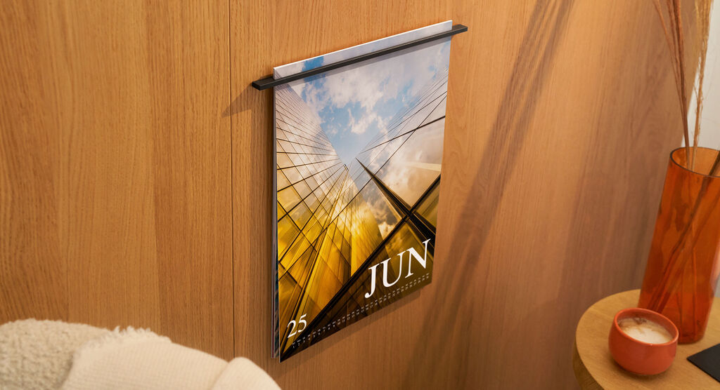 Ein Kalender mit einem modernen Design hängt an einer Holzwand. Der Monat Juni ist hervorgehoben, mit einem klaren Blick auf ein beeindruckendes Gebäude und Himmel.