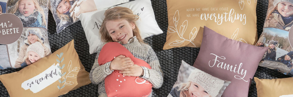 Ein Kind liegt auf Kissen mit persönlichen Fotodrucken und liebevollen Sprüchen.