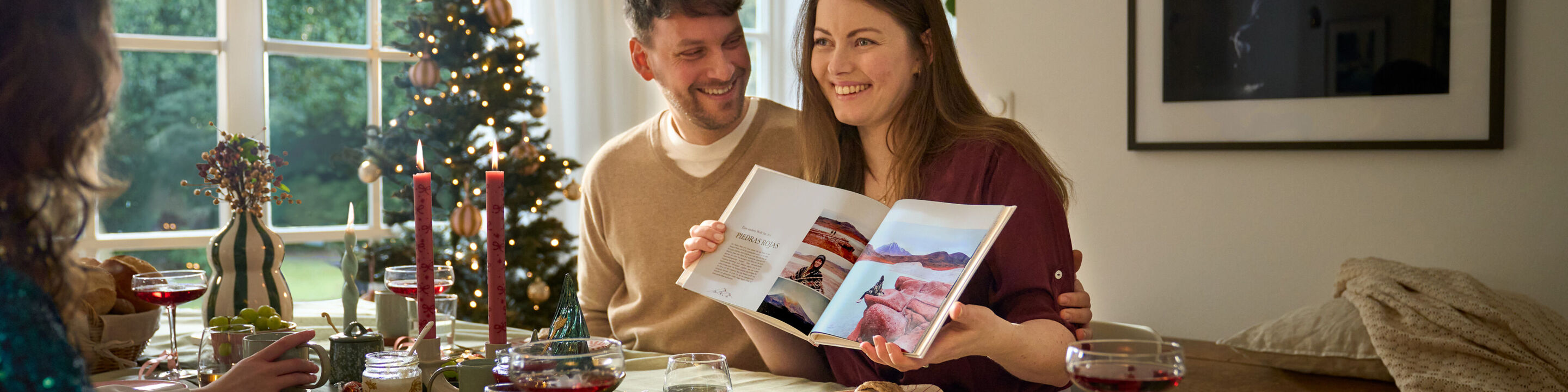 Lächelnde Personen am Tisch betrachten gemeinsam ein CEWE FOTOBUCH.