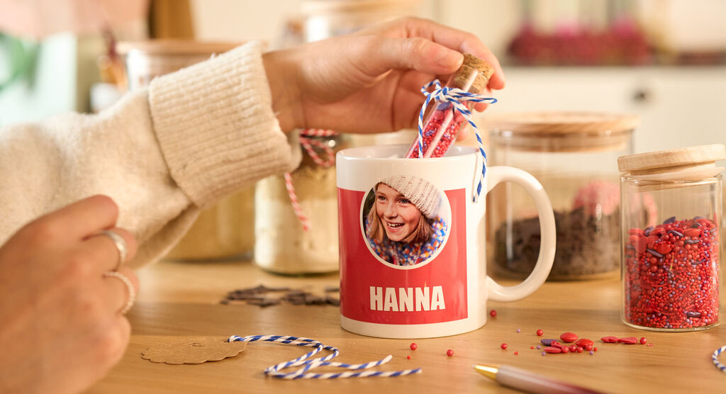 Tasse mit rotem Design und dem Namen Hanna steht zwischen bunten Streuseln und Dekogläsern.