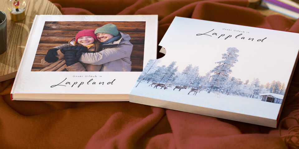 Ein winterlich gestaltetes CEWE FOTOBUCH mit Schuber liegt auf einem Tisch.