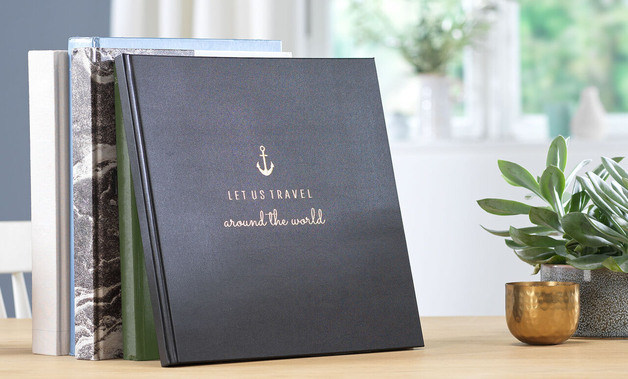 Schwarzes Fotobuch mit dem Titel 'Let Us Travel around the World' auf einem Tisch