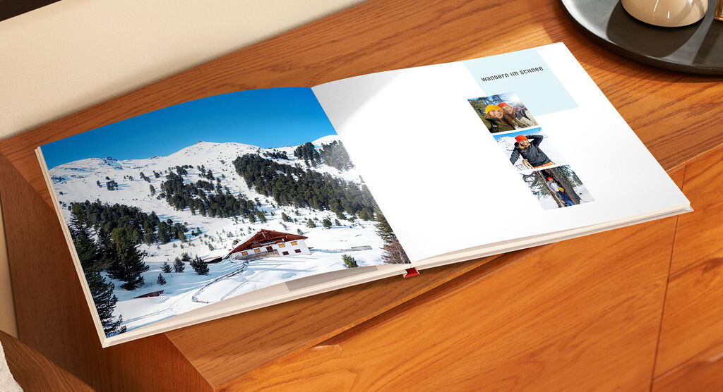 Ein geöffneter CEWE Fotobuch auf einem Holztisch, zeigt wunderschöne Schnee- und Landschaftsbilder.