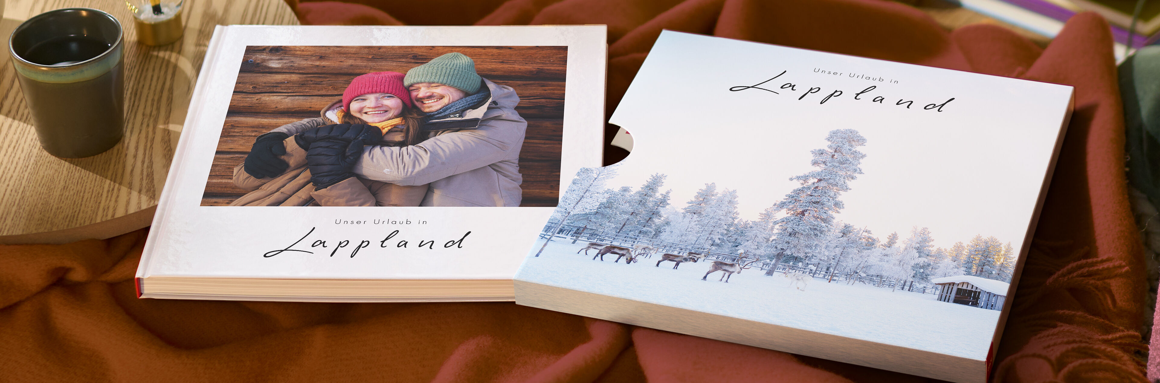 Ein CEWE FOTOBUCH mit Schuber und einer Winterlandschaft aus Lappland mit einem lächelnden Paar.