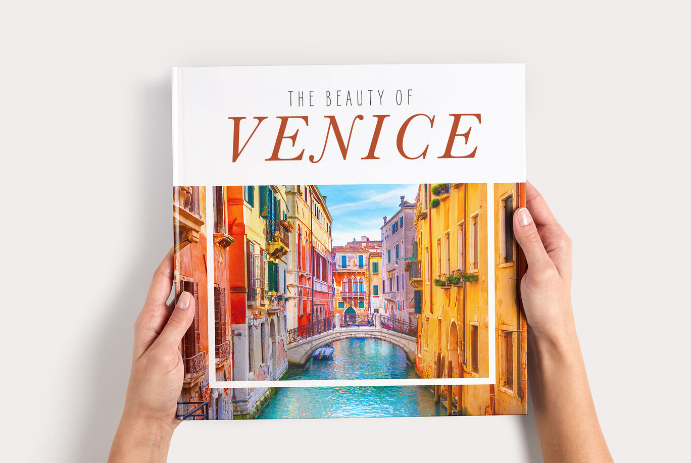 Jemand hält ein CEWE FOTOBUCH mit dem Titel „Venice” und einem Bild von Venedig in den Händen.