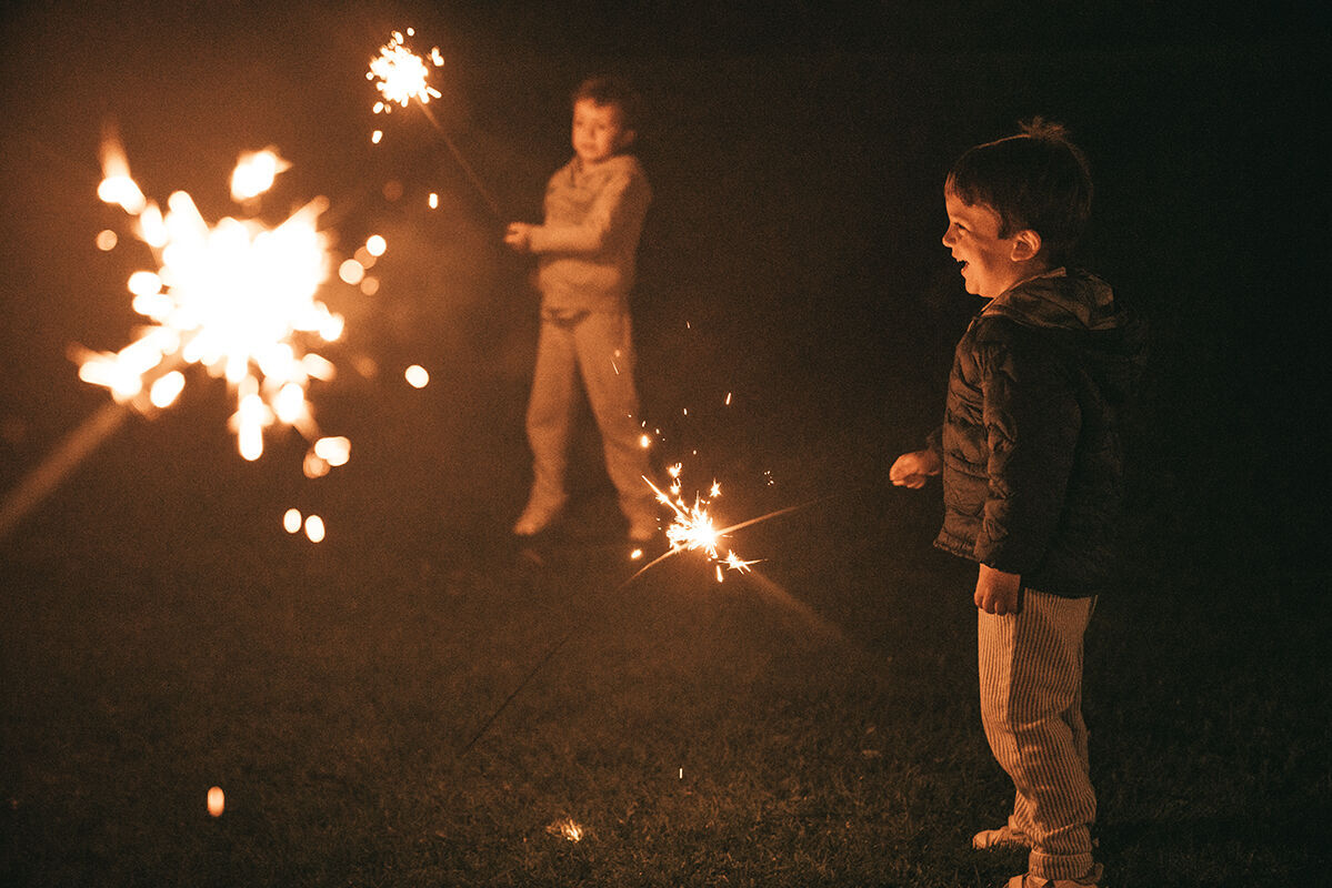 Zwei Kinder spielen mit Wunderkerzen im Dunkeln und strahlen Freude aus