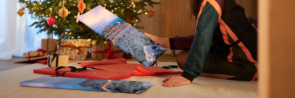Eine Person, die vor einem Weihnachtsbaum sitzt und ein großes Bild betrachtet, während Geschenke um sie herum liegen
