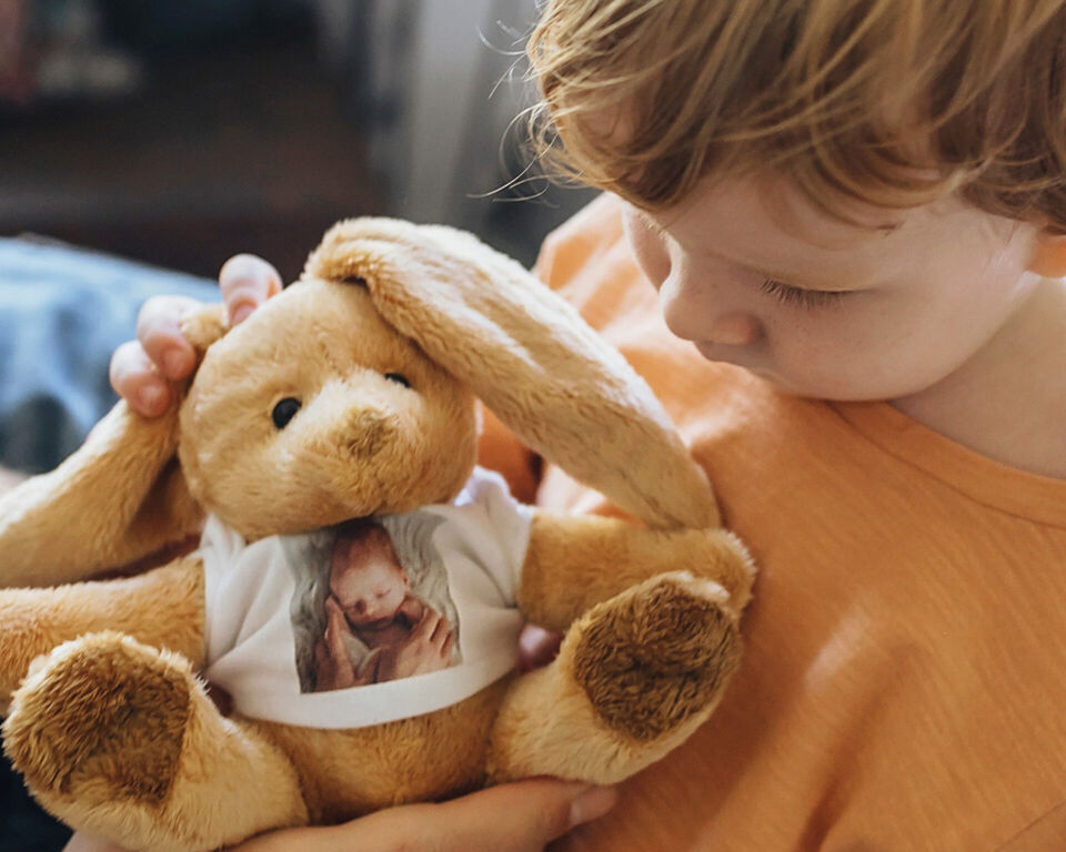 Kind hält einen Kuschelhasen mit Babyfoto auf dem T-Shirt in den Armen.