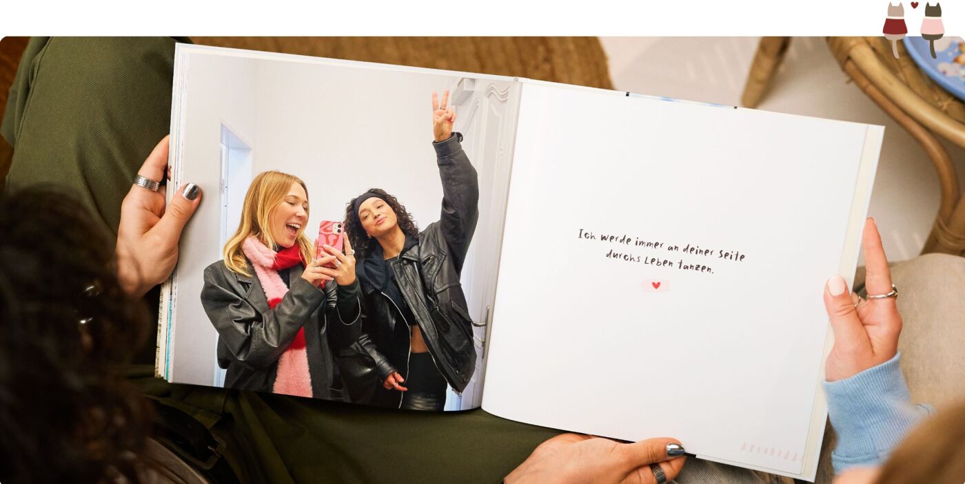 Zwei Freund:innen posieren freudig mit einem CEWE FOTOBUCH.
