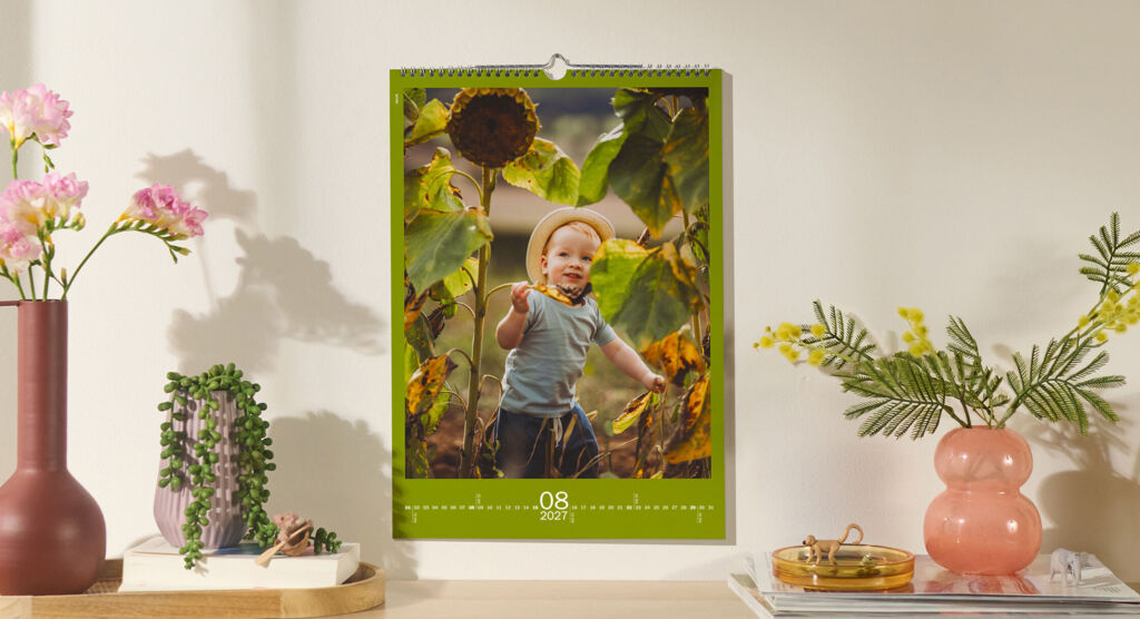 CEWE Fotokalender mit Kind zwischen Sonnenblumen an Wand über Regal mit Blumen und Deko